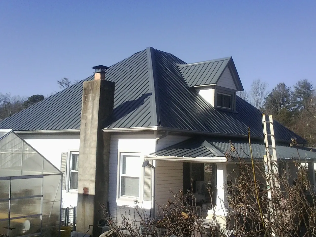 Dark blue standing seam metal roof on a white farmhouse with dormer — Slate & Tile Roof Repair by Roofing Brothers in Whitmire