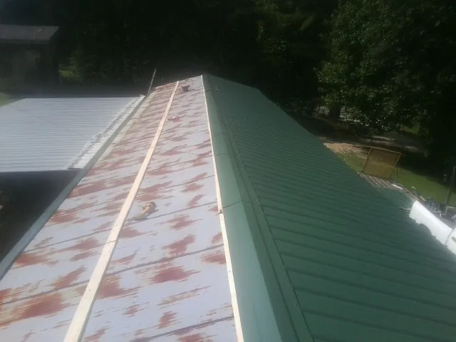 Old rusted panels beside newly installed green metal roofing — Wind Damage Roof Repair by Roofing Brothers in Whitmire