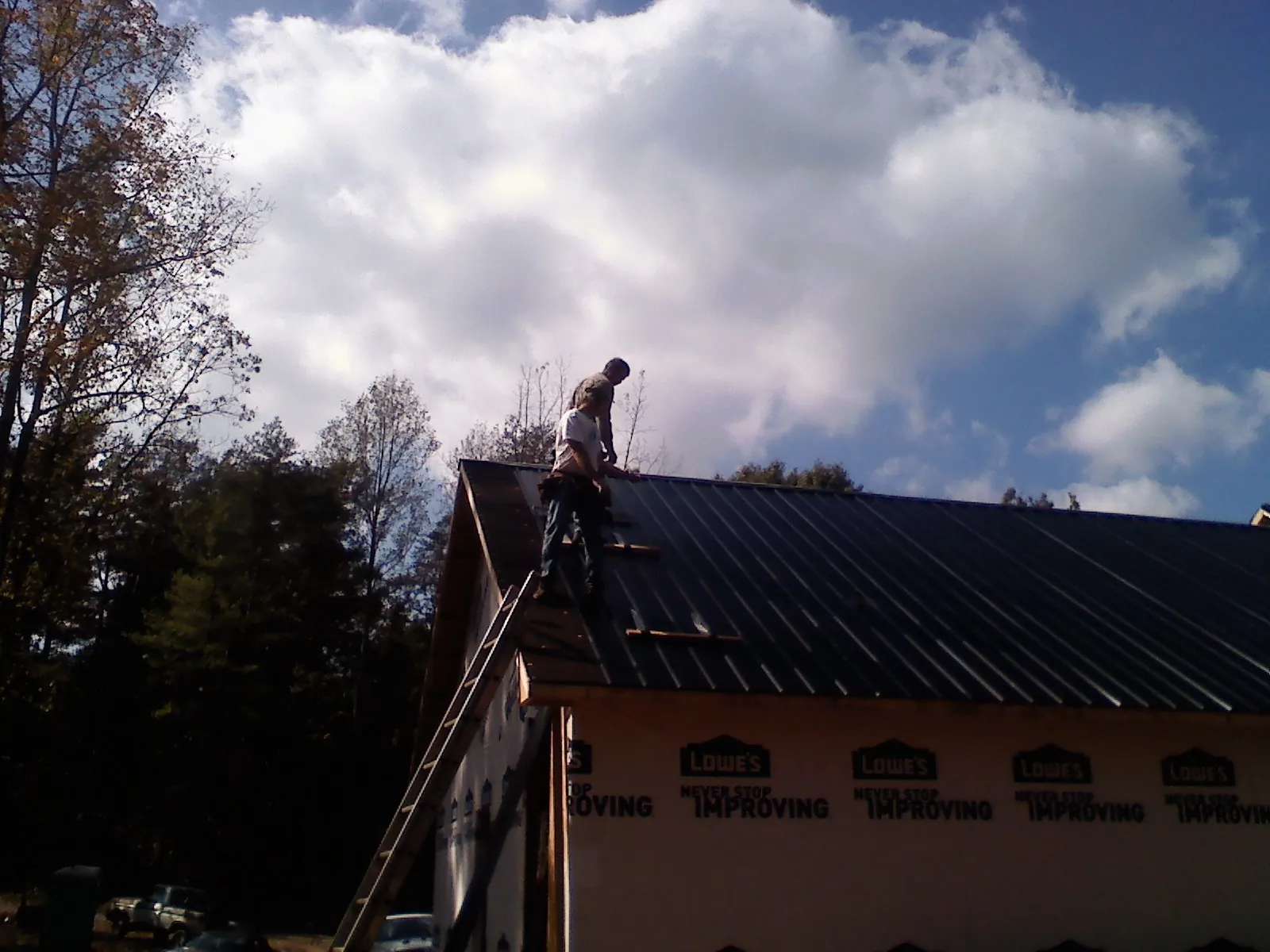 Roofer fastening dark metal panels high against a cloudy sky, from a Roof Inspection job in Whitmire