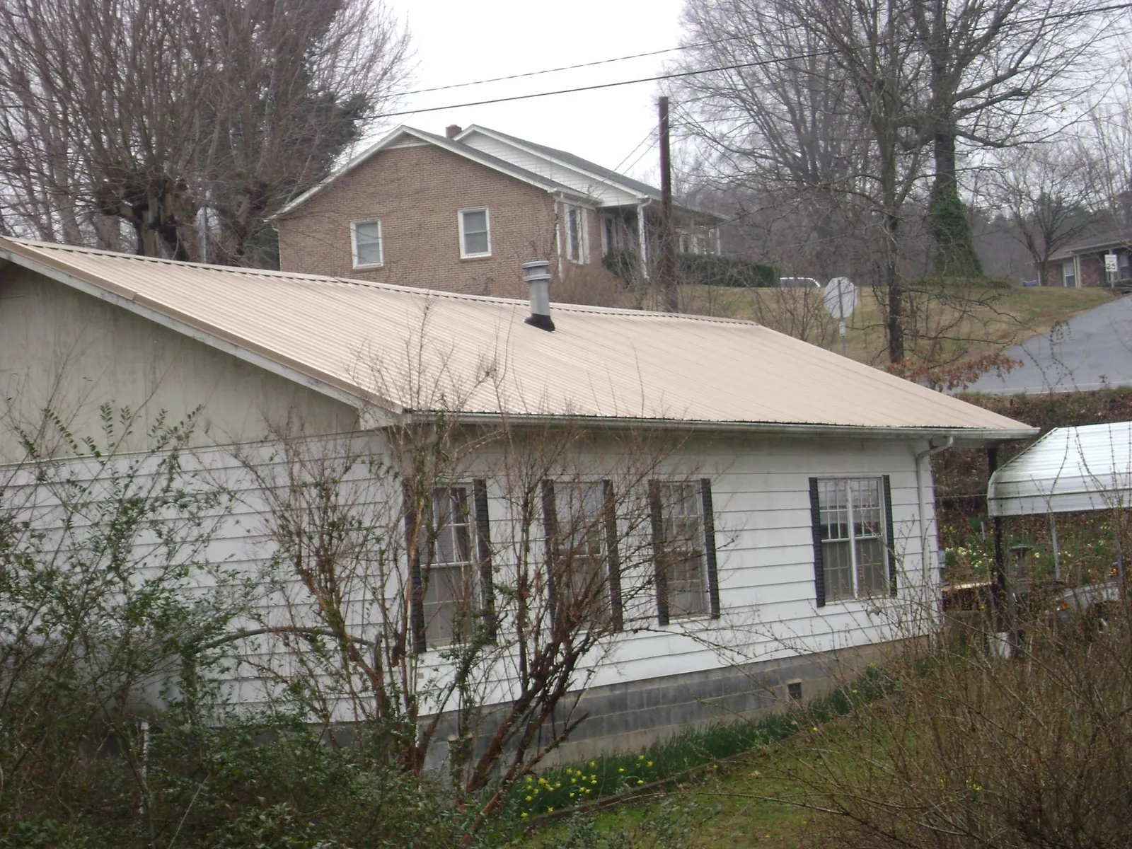 Tan metal roof on a white sided house set into a hillside — Commercial Roofing by Roofing Brothers in Whitmire