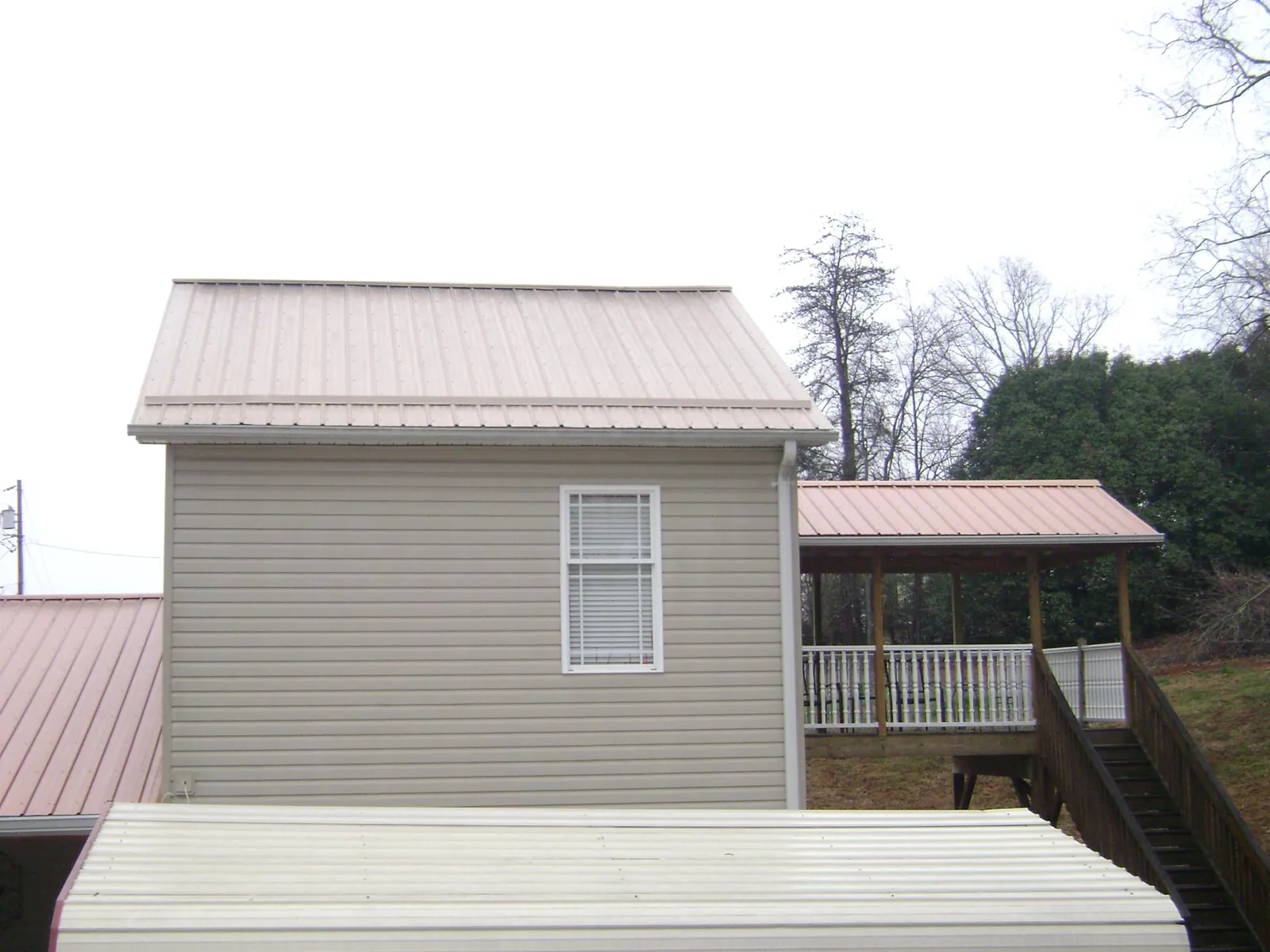Tan metal roofs on a two story addition and attached porch, from a Roof Replacement job in Whitmire